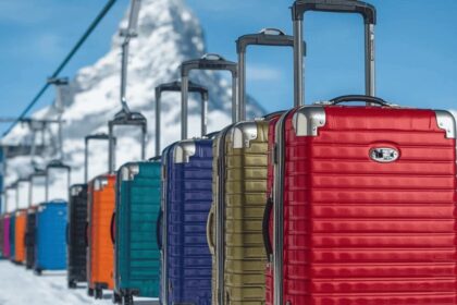 スキーリフトに整然と吊るされ、雪の積もったマッターホルンを背に空を運ばれていく、色とりどりのキャリーバッグ A line of colorful carry-on bags swaying on a ski lift, drifting against the backdrop of the snow-capped Matterhorn peak under a clear blue sky